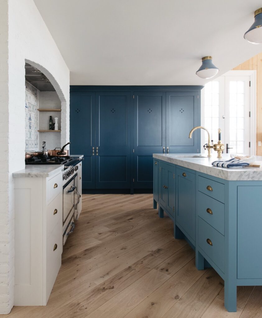 Bespoke kitchen with dark blue cupboard, light blue cabinets, stone walls, and marble countertop