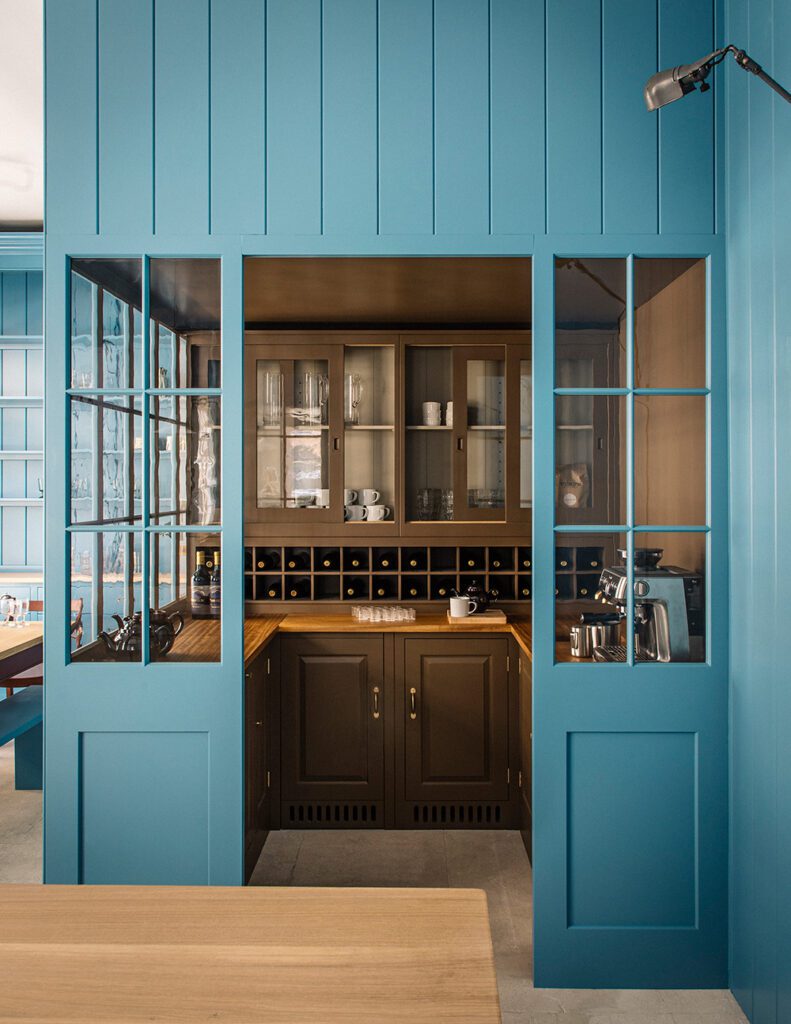 A cozy kitchen nook features rich brown cabinetry with glass doors, surrounded by vibrant blue paneling, showcasing a blend of traditional and modern design.