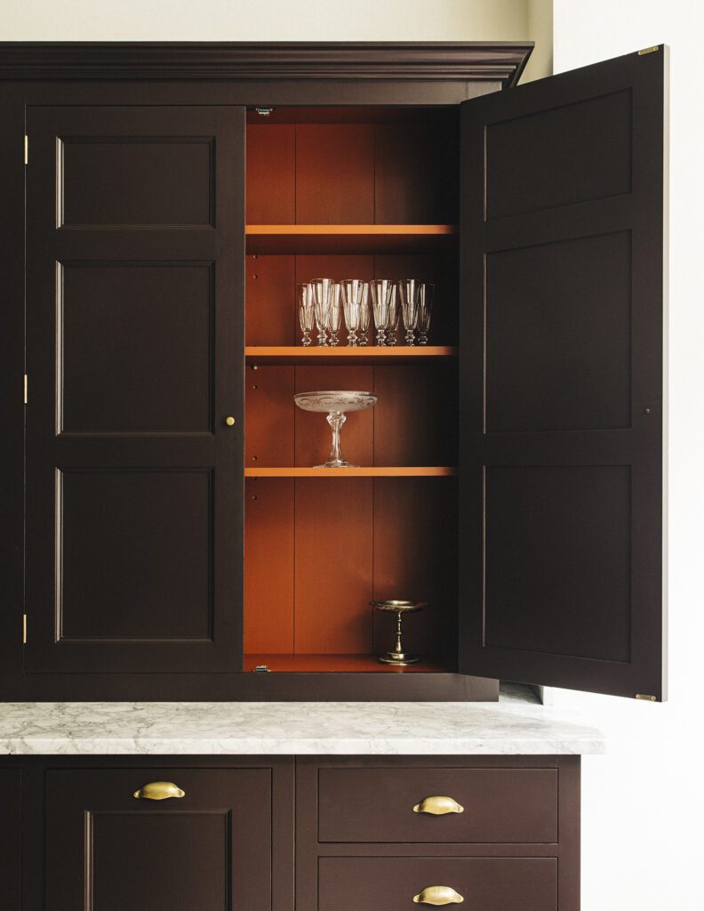 Tall black kitchen cupboard open ajar with glassware inside, brass hardware
