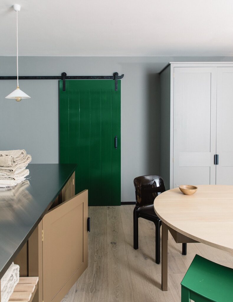 A green sliding door  in room with wood circle table, brown kitchen cabinets, and white cupboard