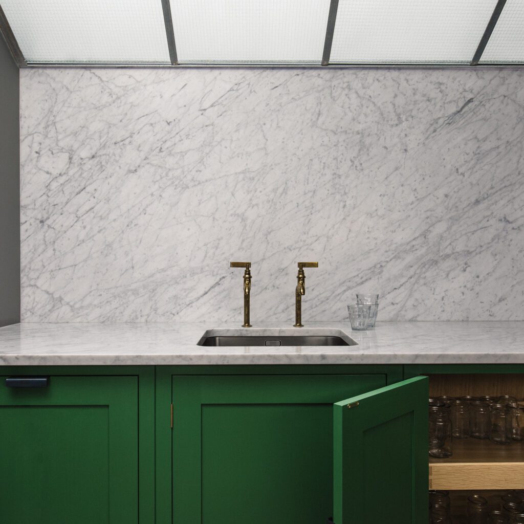 Bespoke marble countertop, bronze faucets, and pickle green cabinets on floor ground