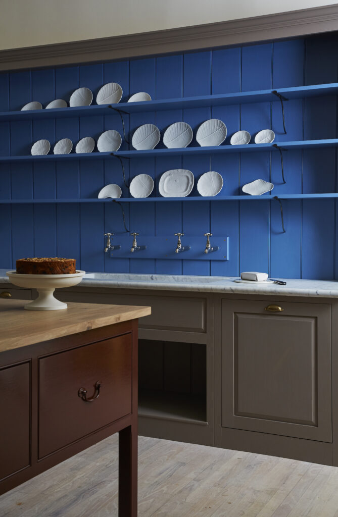 A vibrant blue kitchen wall with hanging plates above a marble sink, brown cabinets, and kitchen island with brown cabinets and a wood countertop