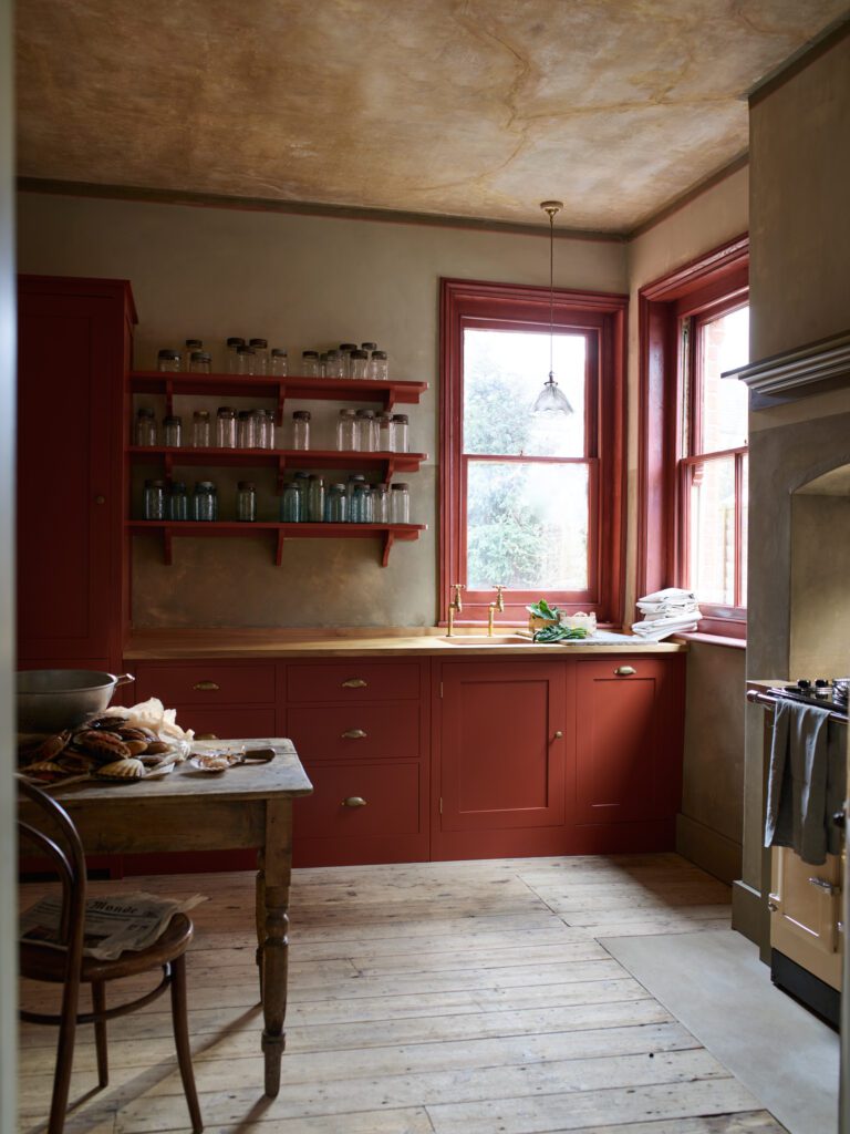 A rustic kitchen featuring red trim and cabinets with wood floors and an open spice rack