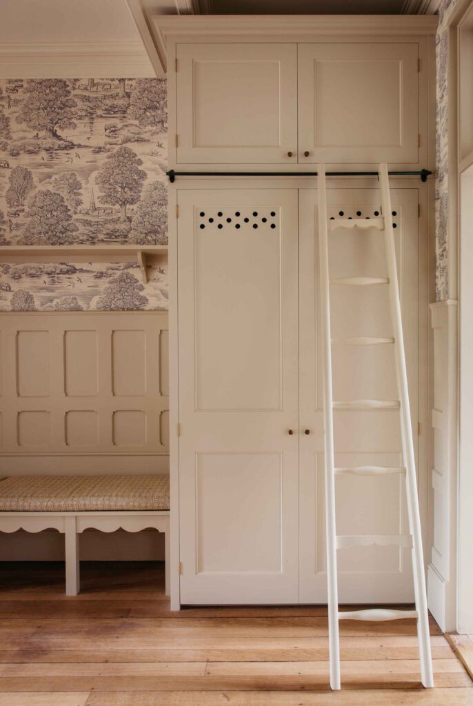 A white cupboard with ladder, next to white bench with expert woodworking design