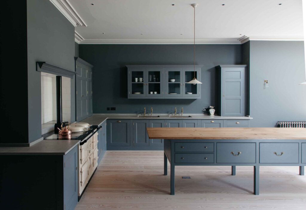 A spacious kitchen with blue cabinetry, wood countertop for island, and a hanging cupboard with cups and plates