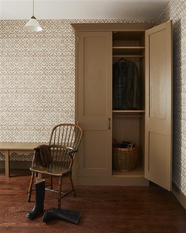 A brown cupboard with one door open, storing clothes next to brown bench and wood chair in center of room