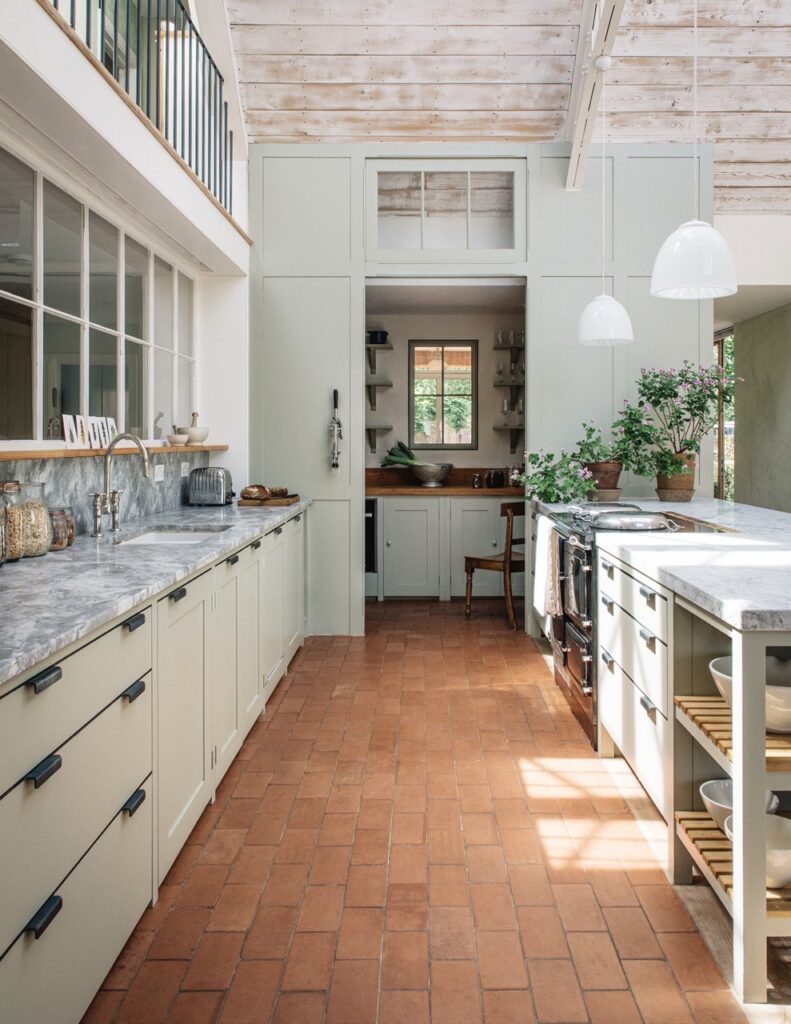 a high-quality bespoke kitchen with Osea-style cupboards in a sage green color and terracotta flooring