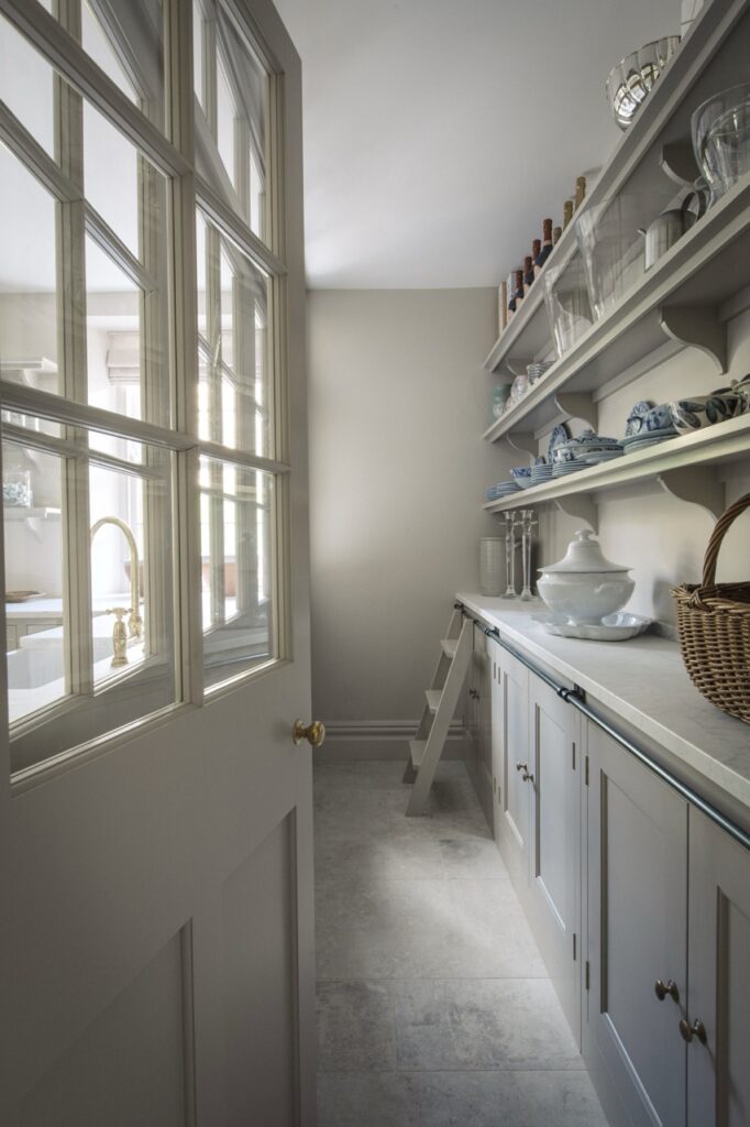 a butlers pantry in a neutral, muted color palette with light gray cabinetry and walls with open shelving above a countertop
