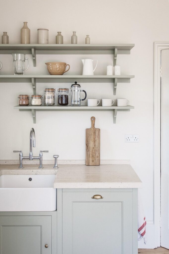 a traditional English-style kitchen with bespoke, shaker-style cabinets with open shelving above a light-colored stone countertop