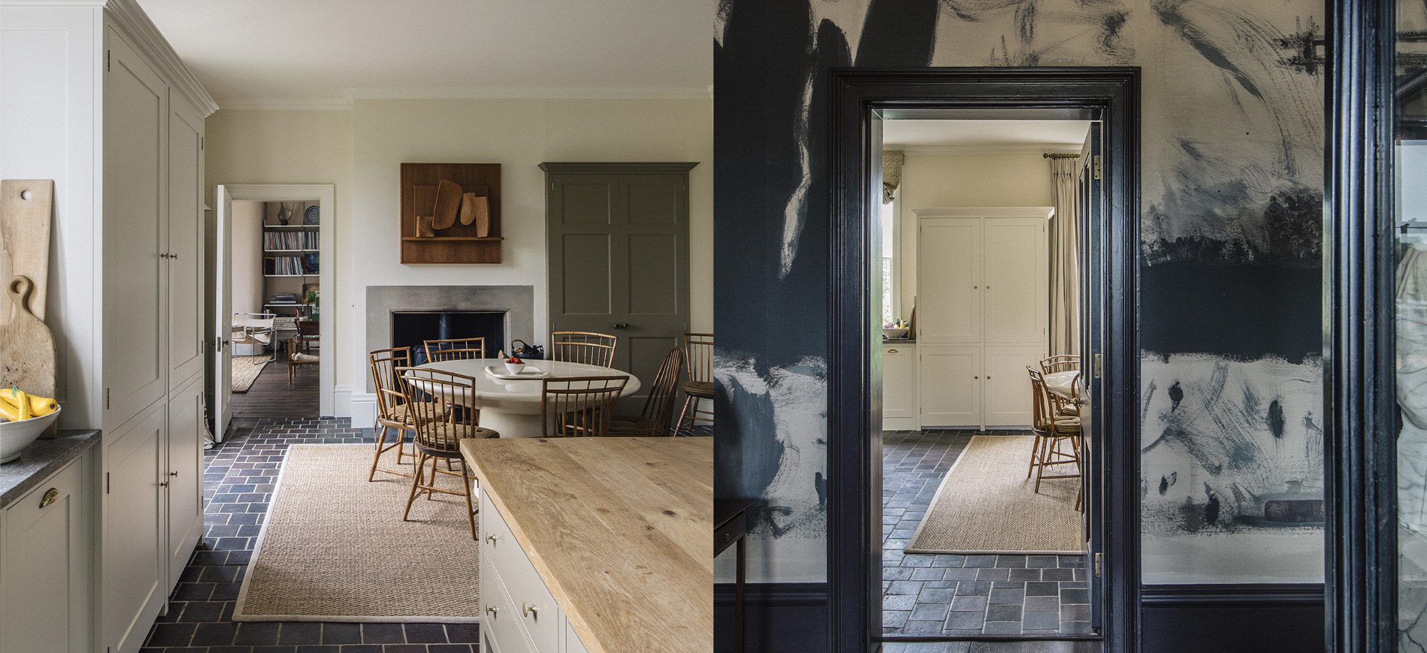  A kitchen and dining area with classic Georgian detailing features cream cabinetry, a wooden dining table with chairs, a fireplace, and a contrasting dark-painted wall with artistic brush strokes.