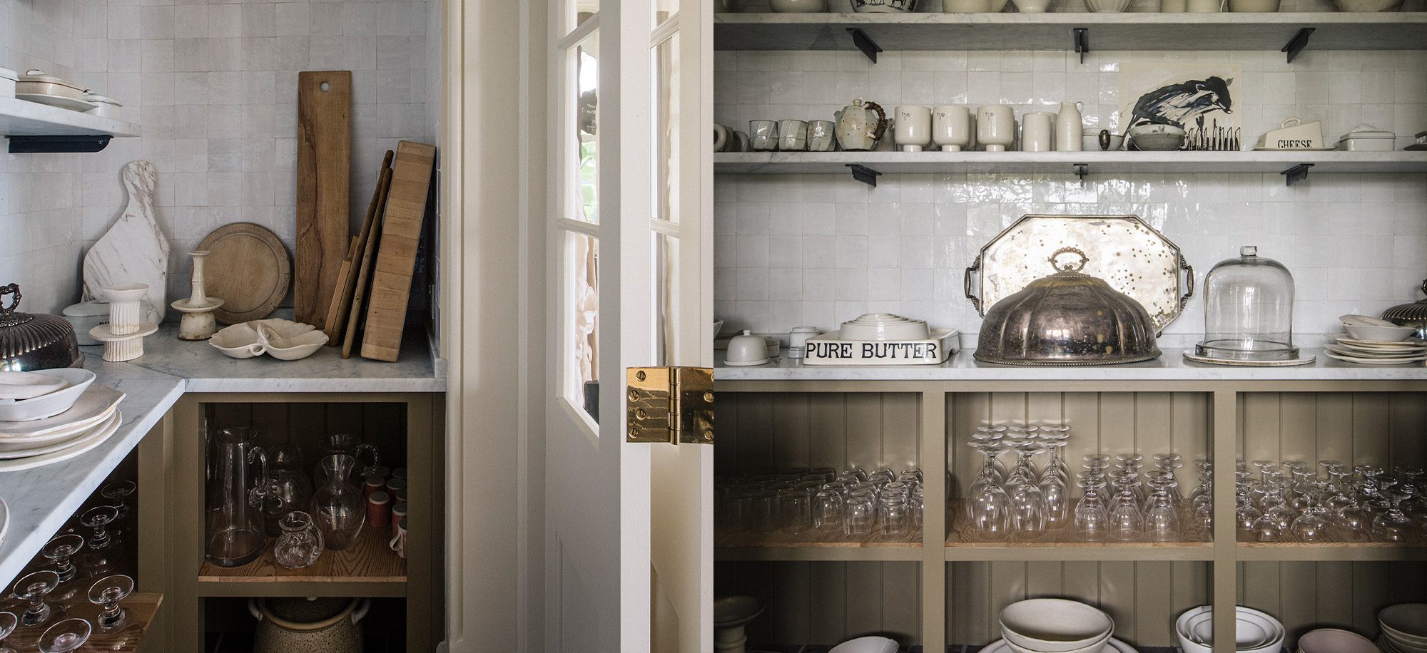  A pantry with cream cabinetry, open shelves displaying white ceramics, glassware, and wooden boards, featuring a marble countertop and a mix of vintage and modern elements.