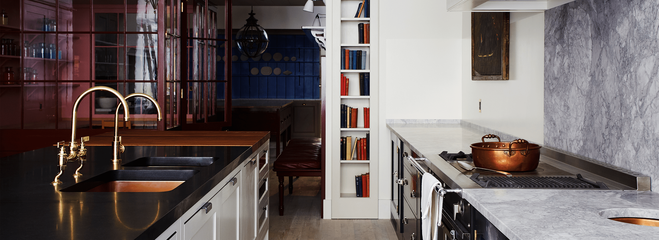 A kitchen with white cabinetry, a dark wood countertop, a built-in bookshelf with colorful books, and a blue-tiled wall in the background.