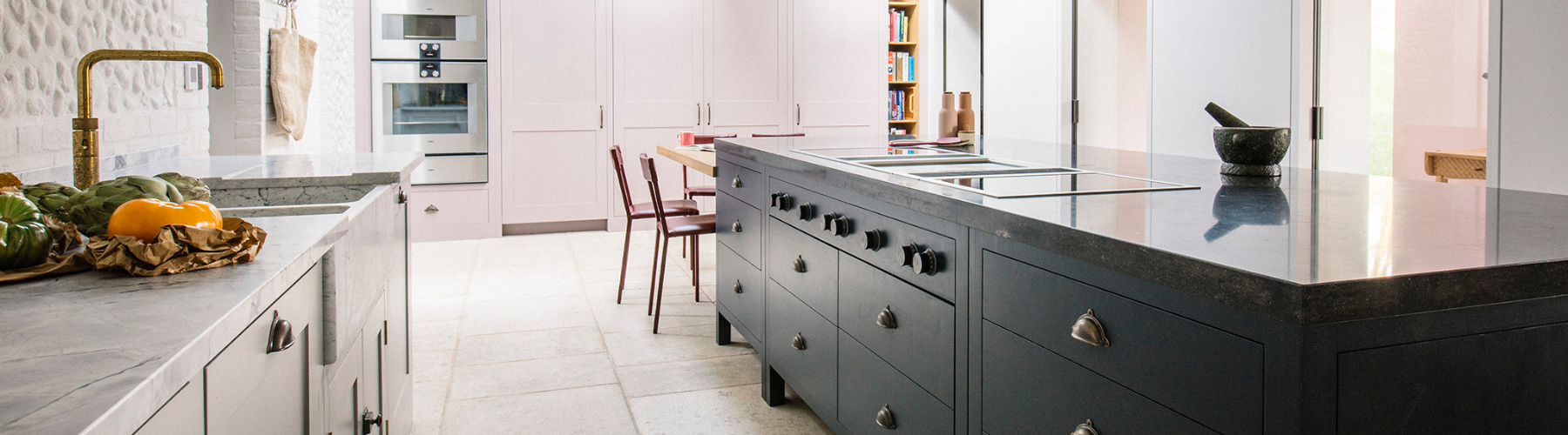 Modern kitchen with a large dark island, marble countertops, brass faucet and integrated cooktop.